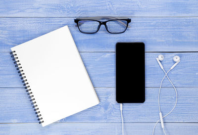 Directly above shot of smart phone with book and eyeglasses on table