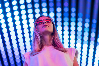 Low angle view of woman wearing sunglasses standing against illuminated ceiling