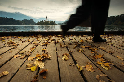 Low section of man standing on footpath by lake against sky