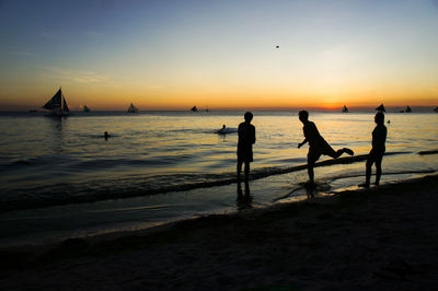 Silhouette people on beach against sky during sunset