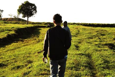 Rear view of man walking on field against clear sky