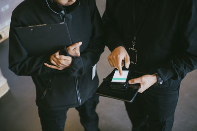 Midsection of female and male colleagues discussing over smart phone at warehouse