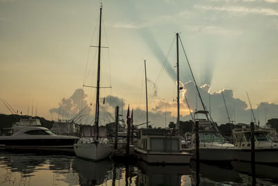 Sailboats moored in harbor at sunset