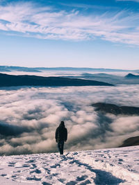 Rear view of man standing on snowcapped mountain against cloudy sky