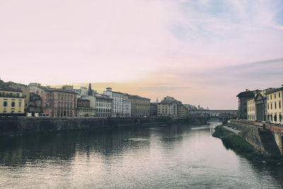 Buildings by river against sky during sunset