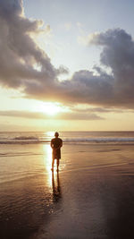 Rear view of man standing on beach against sky during sunset