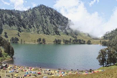 People on lake by mountains against sky