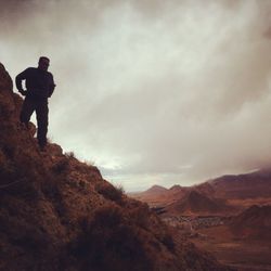 Rear view of woman standing on mountain against cloudy sky