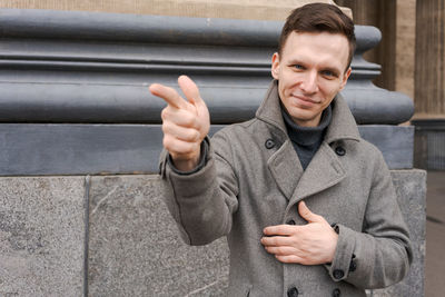 Young man in dark clothes on street. caucasian guy in gray coat, smiles