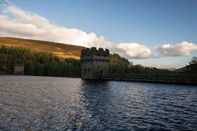 View of building by river against cloudy sky