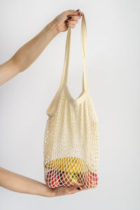 Woman's arms holding a bag with bananas and apples against white background