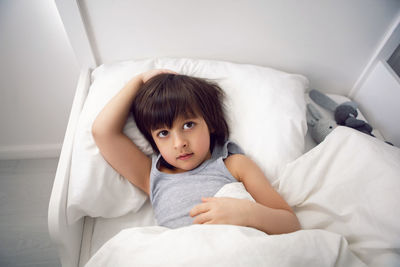 Child boy lies in a white children's bed with a blanket in a room with toys rabbits