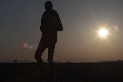 Silhouette man standing on field against sky during sunset