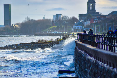 People on sea by buildings against sky