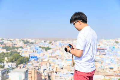 Young man standing against cityscape against clear sky
