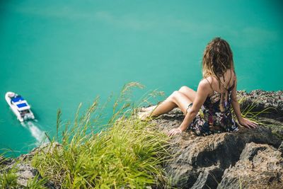 Boy sitting on grass by sea