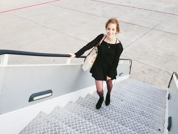 High angle view portrait of woman standing on staircase of airplane at runway