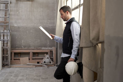 Male contractor analyzing document while standing in building