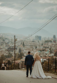 Rear view of couple walking on cityscape against sky