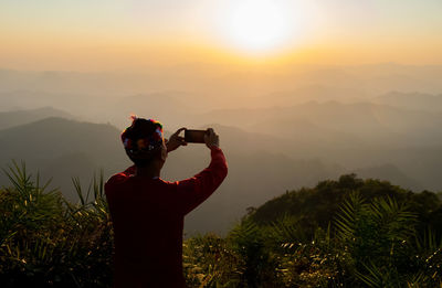 Rear view of man photo graphing during sunset