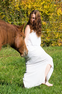 Young woman with horse standing on grassy field against trees during sunny day
