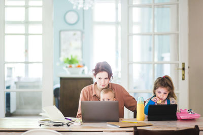 Mid adult woman working on laptop while sitting with children at home