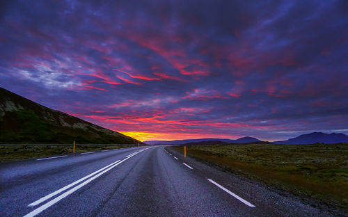 Empty road along countryside landscape at sunset