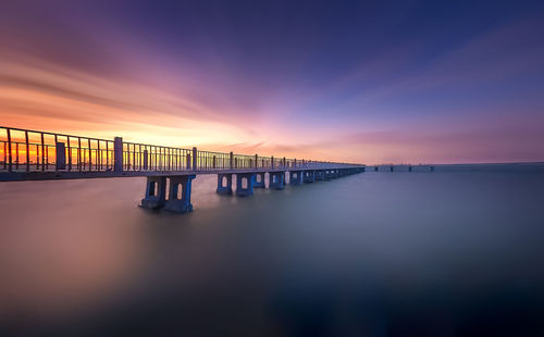 Bridge over sea against sky during sunset