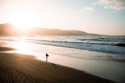 Silhouette person at beach against sky during sunset