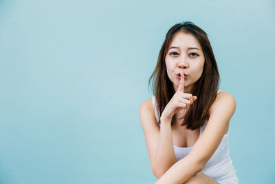 Close-up portrait of young woman with finger on lips against blue background