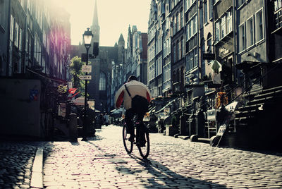 Rear view of man riding bicycle on street amidst buildings in city