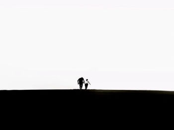 Silhouette people walking against clear sky