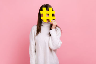 Young woman standing against pink background