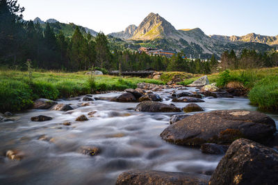 Stream flowing through rocks in river against sky