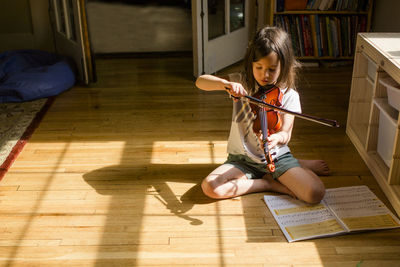 A small girl sits on floor playing violin in front of open music book