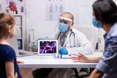 Doctor wearing mask showing virus in digital tablet at hospital
