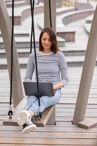 Woman with laptop sitting on swing