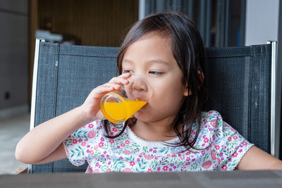 Girl having orange juice while sitting on chair