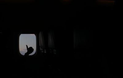 Silhouette hand showing thumbs up by window in airplane