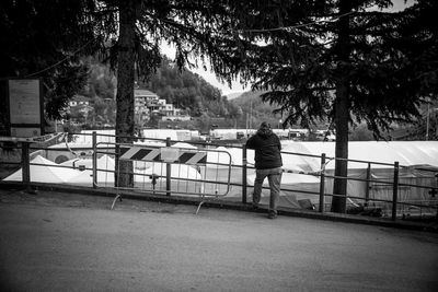 Rear view of man standing on railing against trees