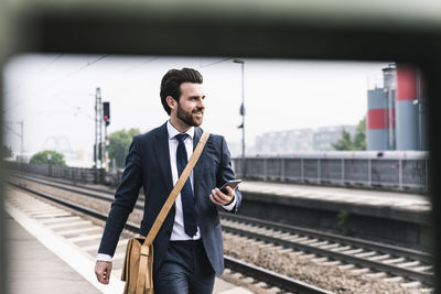 Smiling businessman with cell phone walking at the platform
