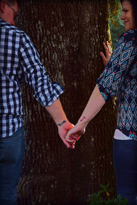 Close-up of couple holding hands on tree trunk