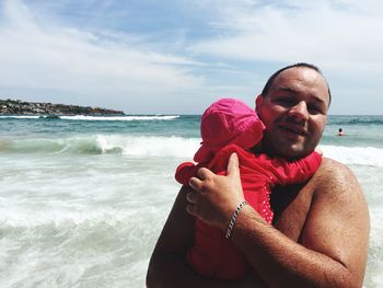 Portrait of smiling father holding daughter at beach on sunny day