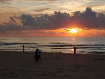 People on beach against sky during sunset