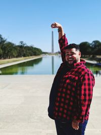 Portrait of smiling man standing at riverbank against sky