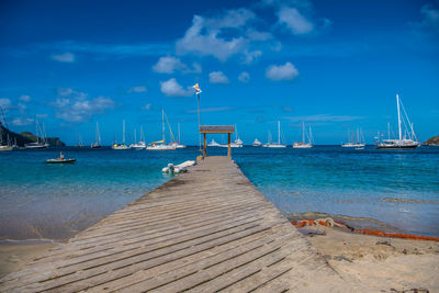 Sailboats moored at harbor against blue sky