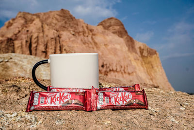 Coffee cup on rock against sky