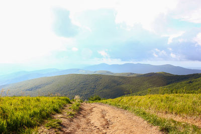 Dirt road amidst field against sky