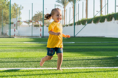 Cute smiling little girl running across green sports field.