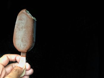 Close-up of hand holding ice cream against black background